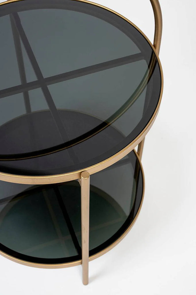 Introducing Side Table Calli a luxurious addition to your interior design. Made with an elegant, gold lustre iron frame and two tempered glass table tops, it adds a touch of glamour to any room. Use the curved handle to easily move it and save on floor space. Perfect for sipping cocktails next to an equally splendid accent chair.