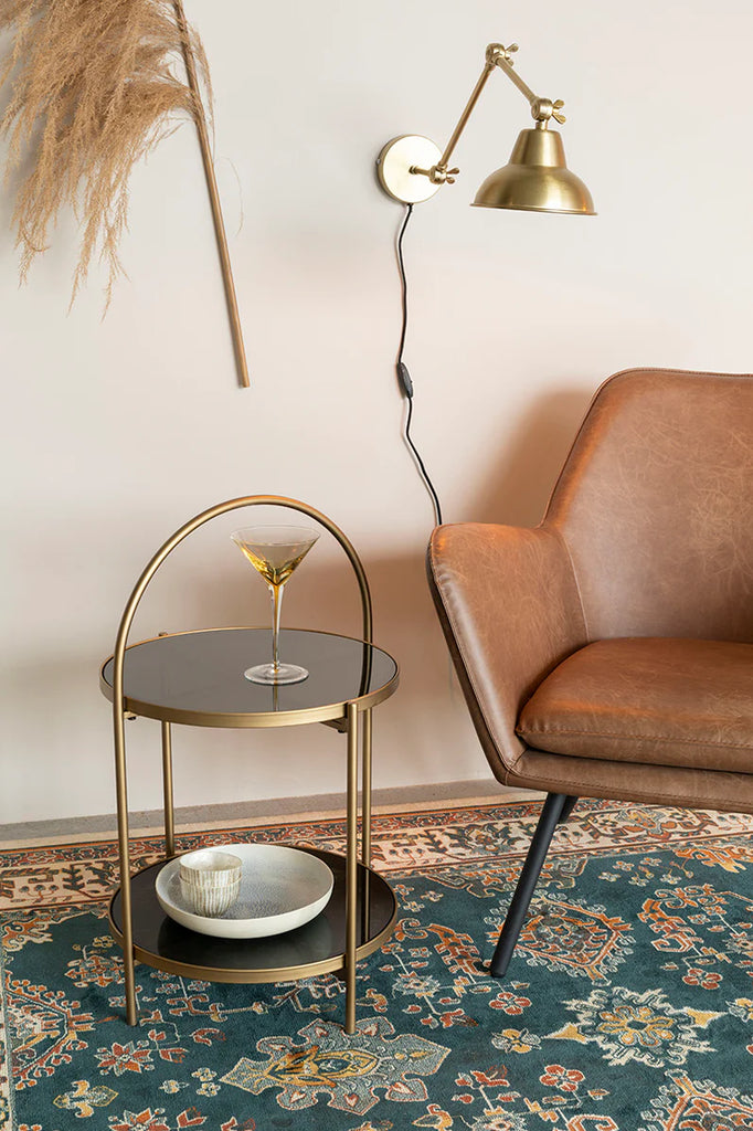 Introducing Side Table Calli a luxurious addition to your interior design. Made with an elegant, gold lustre iron frame and two tempered glass table tops, it adds a touch of glamour to any room. Use the curved handle to easily move it and save on floor space. Perfect for sipping cocktails next to an equally splendid accent chair.