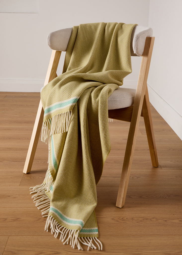 draped over a chair Inspired by the soft sands and refreshing hues of Silver Strand, the Foxford Silver Strand Lambswool and Cashmere Throw is a perfect blend of luxury and comfort. Woven in our historic mill in County Mayo, this exquisite throw combines lambswool's warmth with cashmere's softness. Featuring a citrus-toned herringbone weave with a delicate mint green stripe near the fringe,