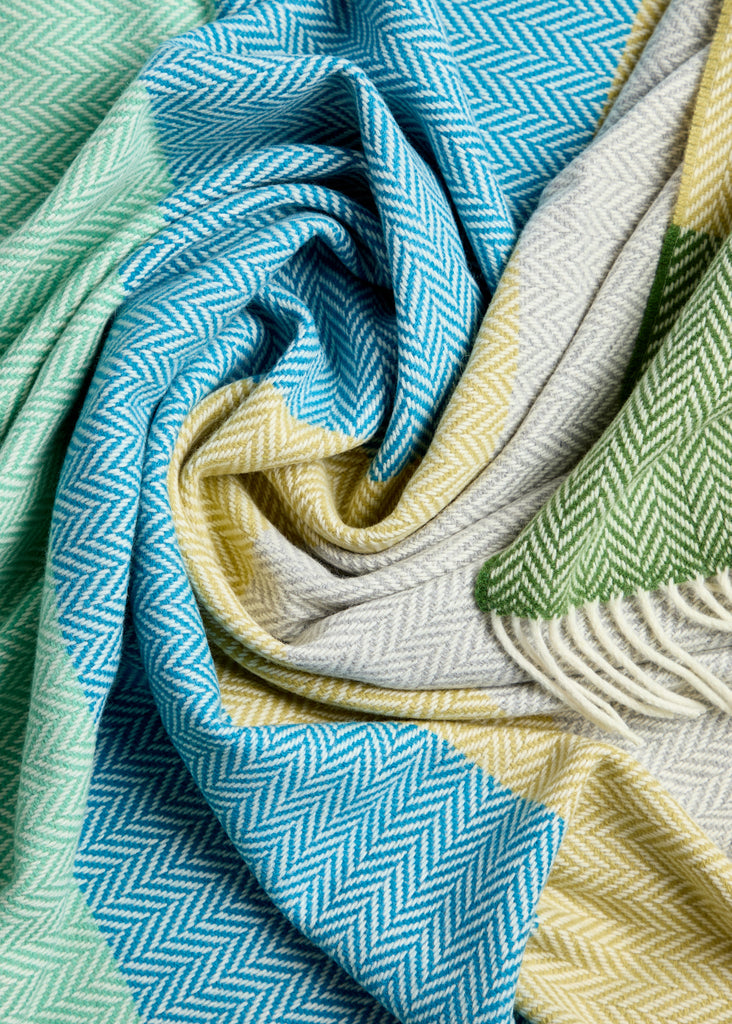 Luxurious Foxford Garavogue Cashmere and Lambswool Throw Featuring a vibrant herringbone pattern in blues, greens, and yellows, with soft fringed edges. Woven in Foxford’s historic mill in County Mayo, Ireland.