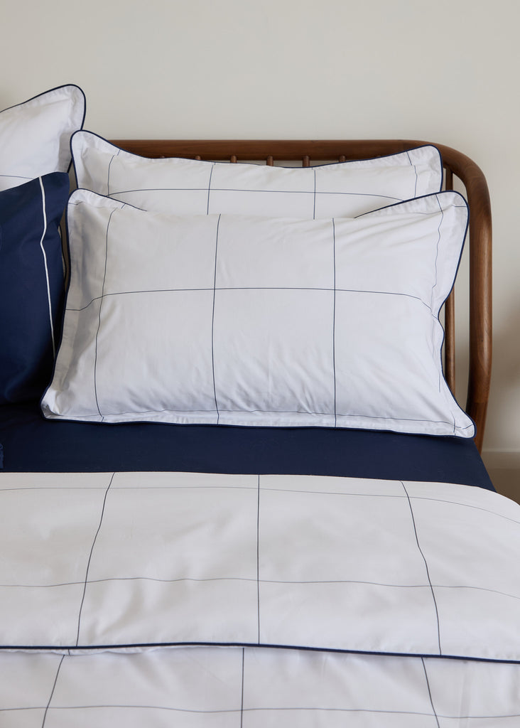 The Foxford Navy Windowpane Oxford Pillowcase features a classic navy windowpane print and is part of a crisp white bedding set. With a thread count of 300, this bedding is expertly woven in Portugal and designed by the renowned designer Helen McAlinden. It brings a touch of timeless elegance to any bedroom decor—a single pillowcase.