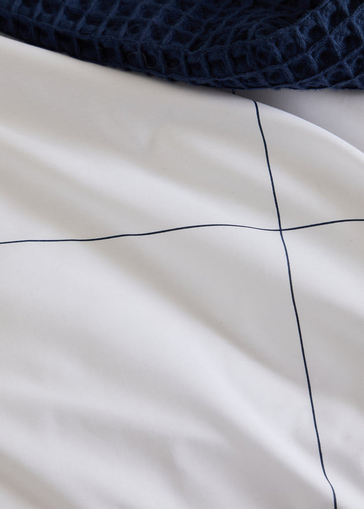 The Foxford Navy, Windowpane Pillowcase Set, features a traditional navy windowpane design and is part of a pristine white bedding collection. With a 300 thread count, this bedding is skillfully crafted in Portugal and conceptualized by esteemed designer Helen McAlinden, adding timeless sophistication to any bedroom. Two pillowcases.