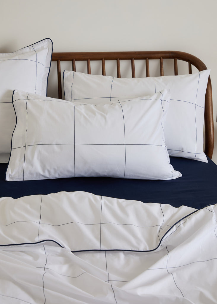 The Foxford Navy, Windowpane Pillowcase Set, features a traditional navy windowpane design and is part of a pristine white bedding collection. With a 300 thread count, this bedding is skillfully crafted in Portugal and conceptualized by esteemed designer Helen McAlinden, adding timeless sophistication to any bedroom. Two pillowcases.